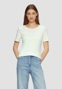 T-shirt blanc à manches courtes avec un col rond, texture lisse et design ajusté, porté avec un jean en denim bleu clair.