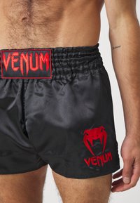 Schwarze Satinshorts mit rotem, gesticktem "Venum"-Logo am Bund und Bein. Sie verfügen über einen elastischen Bund für Flexibilität.