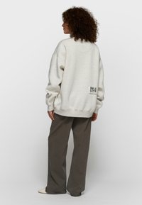 Sudadera oversize de color gris claro con acabado texturizado y puños acanalados, con un parche negro con las palabras "SMILE LOVE TODAY" en la parte baja de la espalda.