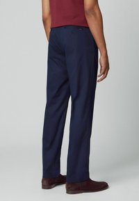 Navy broek met een ontspannen pasvorm, met een gladde textuur, ceintuurlussen en een achterzak. Gecombineerd met bruine suède schoenen.