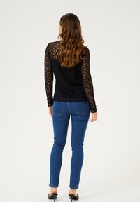 Top en dentelle noire à manches longues, avec un motif texturé. Associé à un jean slim bleu et des chaussures à talons noires.