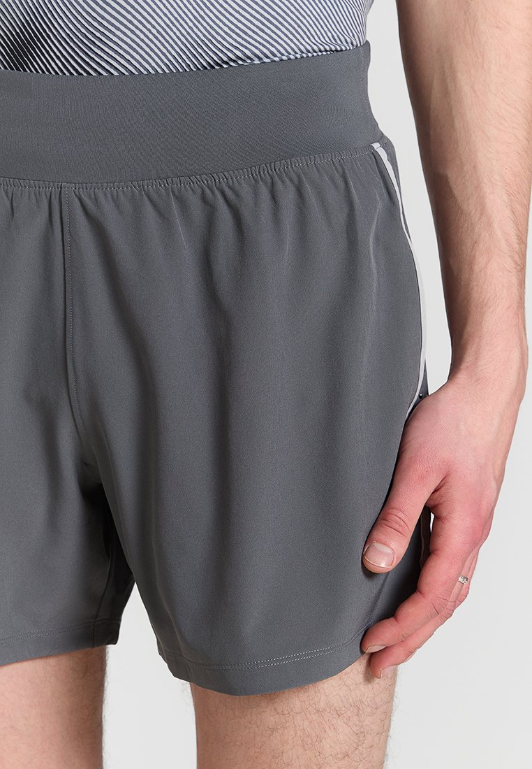 Pantaloni corti sportivi grigi con vita elastica, caratterizzati da una trama liscia e dettagli laterali. Il tessuto è leggero e traspirante.
