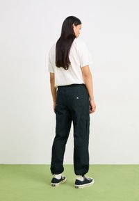 Pantalones cargo verde oscuro con bolsillos laterales, tobillos ajustados y un ajuste relajado, combinados con una camiseta blanca de mangas cortas y zapatillas negras.