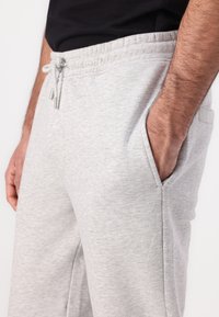 Light gray cotton sweatpants with elastic waistband, drawstring, and side pockets. Smooth texture and relaxed fit. Simple, functional design.