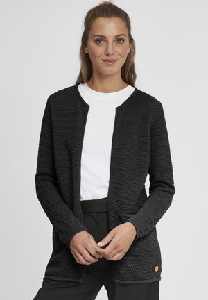 Black textured cardigan with a round neckline, open front, and two pockets. Worn over a white shirt, featuring subtle logo detail.