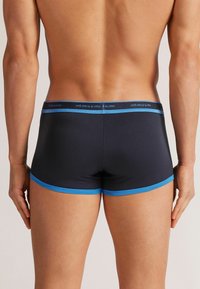 Schwarze Herrenboxershorts mit einem blauen Gummibund und Besatz, aus einem weichen Material für Komfort. Ansicht von hinten.