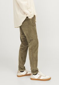 Olive green corduroy pants with a textured finish, paired with casual white sneakers featuring beige accents and a gum sole.