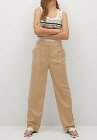 Pantalon large beige avec plis sur le devant, associé à un débardeur en tricot multicolore avec des rayures horizontales. Tissu lisse et léger.