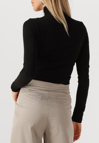 Zwarte lange mouwen coltrui gecombineerd met lichtbeige hoge taille broek. Glad materiaal, slim fit ontwerp, minimale zichtbare naden.