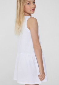 Robe blanche sans manches avec une jupe évasée, fabriquée en coton doux. Présente un design simple et une texture lisse, adaptée pour un usage décontracté.