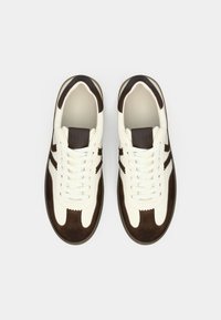 Valged nahast tossud pruunide seemisnahast detailidega, millel on ümar ninaosa, lamedad paelad ja polsterdatud krae mugavuse tagamiseks.