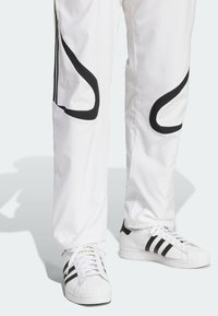 Vita idrottsbyxor med svarta accenter och böjda mönster, matchade med vita sneakers med svarta ränder och en texturerad gummisula.