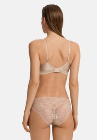 Reggiseno nudo con spalline regolabili, dettagli in pizzo e chiusura con gancio. Slip trasparenti in pizzo coordinati con un intricato motivo floreale sul retro.