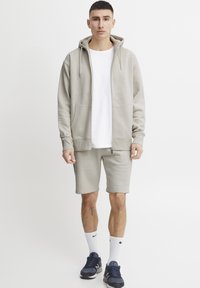 Lys grå hettegensar med glidelås, kombinert med lys grå shorts. Hvit t-skjorte under, marineblå joggesko og hvite sokker.