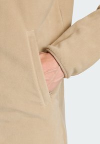 Fleece jack in lichtbeige met een gestructureerde oppervlakte, voorzien van een zijzak en een manchetontwerp voor de mouwen.