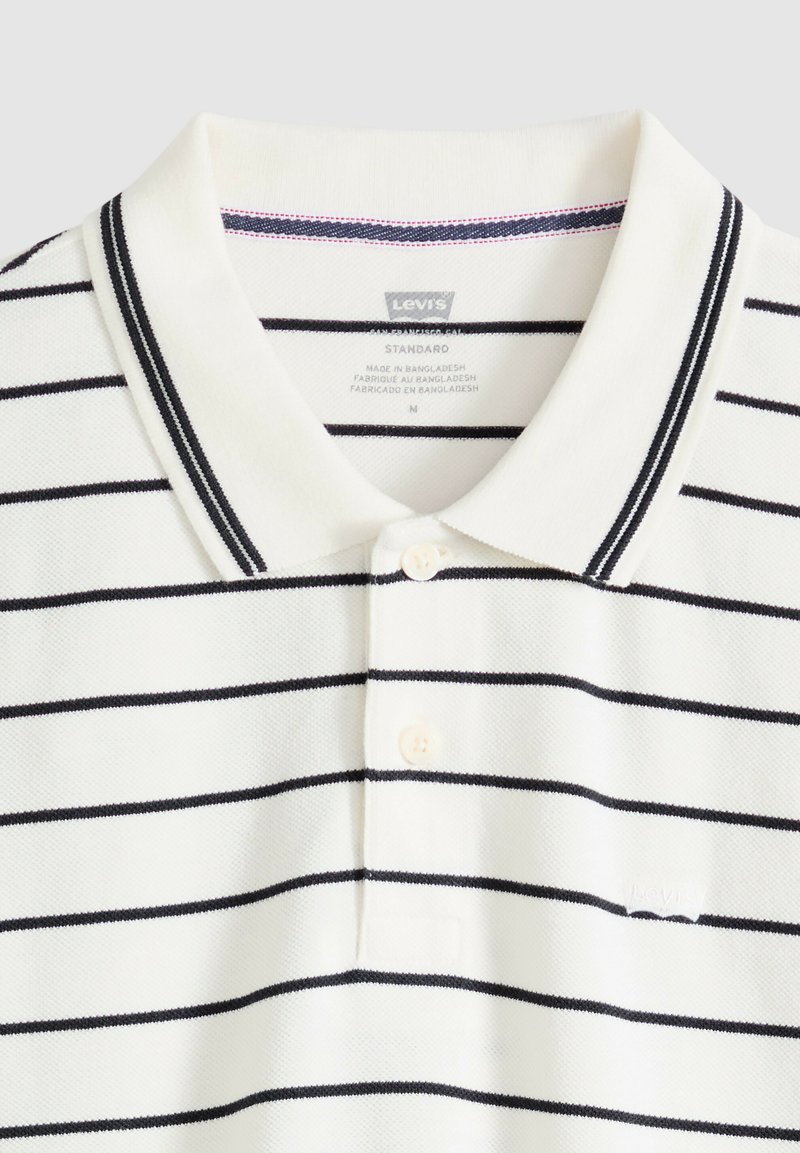 Polo blanco de Levi's con rayas horizontales negras, tapeta con dos botones y cuello con detalles de ribete negro.