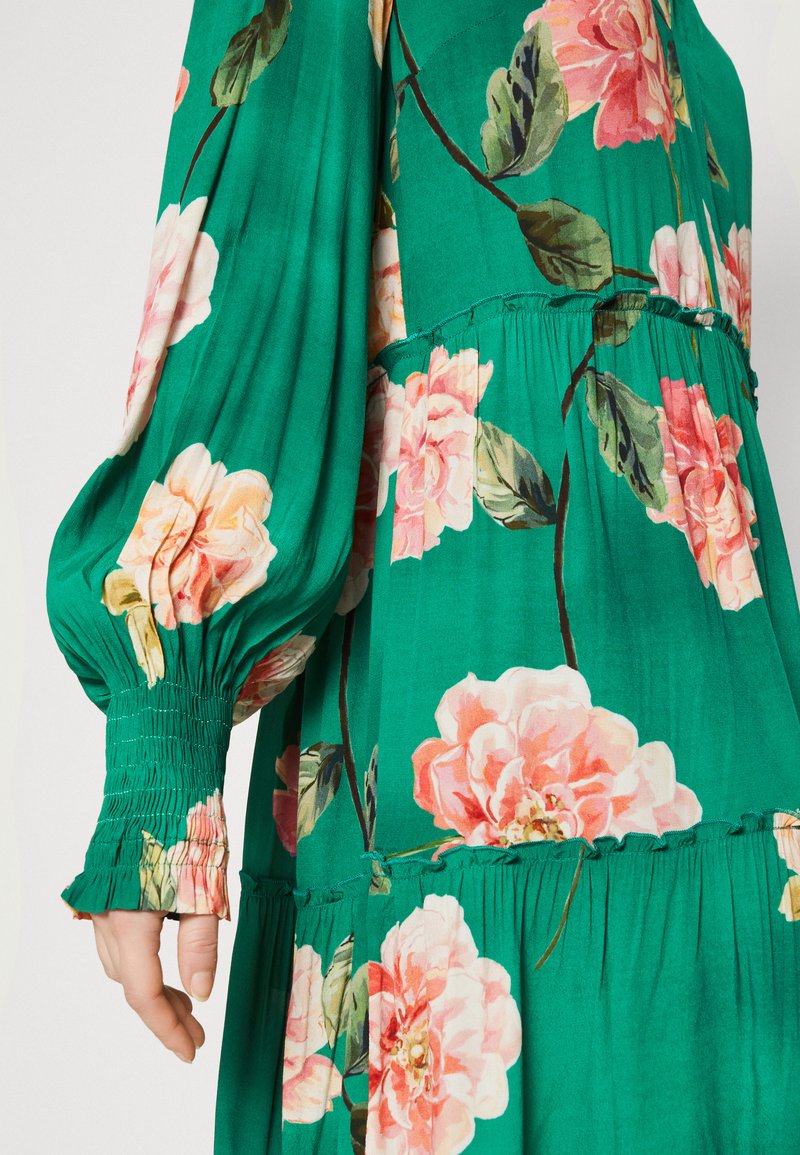 Grünes Blumenkleid mit pinken Blumen, plissierten Ballonärmel und gerafften Stufen. Hergestellt aus leichtem Stoff mit glatter Textur.