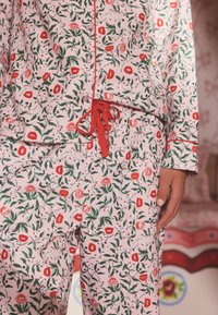 Floral pajama set in soft fabric featuring a pink background with red lips and green leaves. Includes a drawstring waist and button details.