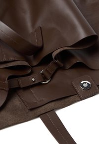 Bruine leren tas met een gladde textuur, voorzien van een schouderband, metalen hardware en een suède voering. Inclusief een kenmerkende drukknoopsluiting.