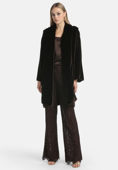 Zwarte fluwelen jas met open voorkant, gelaagd over een bruine satijnen top en bordeauxkleurige kanten flared broek, featuring ingewikkelde bloemmotieven en gegolfde randen.