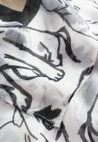 Tissu léger avec un motif abstrait noir et gris sur fond blanc. Les bords présentent une finition délicate en couture.