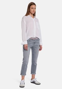 Chemise blanche à manches longues et à boutons avec une poche, portée avec un jean gris clair retroussé et des baskets noir et blanc. Tissu lisse, look décontracté.