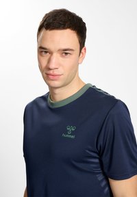 Marine sportshirt met groene kraag en logo. Korte mouwen, zachte textuur en subtiele glans. Accentueert met groene strepen op de schouders.
