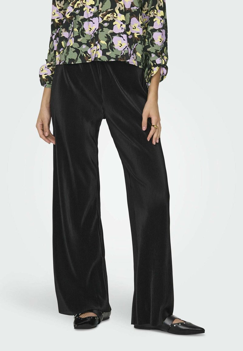 Pantalones anchos de pana negra con canalé vertical, textura suave y un ajuste relajado, combinados con zapatos planos negros de punta puntiaguda.