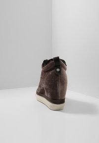 Braune Wildleder-Ankle-Boots mit Kunstfellfutter, klobigem Absatz und einem schwarzen Riemen an der Rückseite. Strukturierte Oberfläche mit einer weißen Sohle.