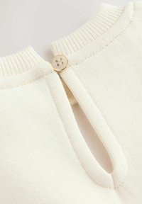 Krémový pletený top s okrúhlym výstrihom, rebrovanými okrajmi a otvormi na chrbte so zlatým gombíkom na zapínanie. Mäkká textúra a jednoduchý dizajn.