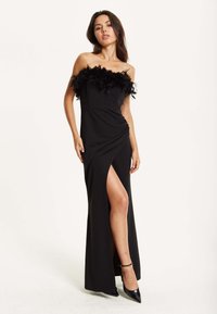 Black evening gown with off-the-shoulder feathered detailing, fitted bodice, and thigh-high slit design. Smooth fabric, elegant silhouette.