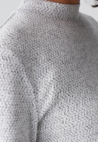 Szary, teksturowany sweter z dzianiny z wysokim kołnierzem. Charakteryzuje się subtelnym, nakrapianym wzorem oraz miękkim, przytulnym wyglądem.