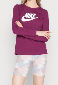 Lila långärmad Nike-tröja med vitt logga, kombinerad med cykelshorts i rosa och blått mönster som har en liten rosa logga.