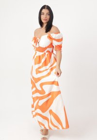Maxikleid in Orange und Weiß mit schulterfreien Ärmeln, gerafftem Oberteil und gewelltem Streifenmuster; der Stoff wirkt leicht und fließend.