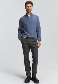 Vyriškas pusiau užtraukiamas tamsiai mėlynas megztinis iš minkštos medžiagos, derinamas su tamsiai pilkomis kelnėmis. Megztinis turi užtrauktuką ir laisvą siluetą. Juodi batai papildo išvaizdą.