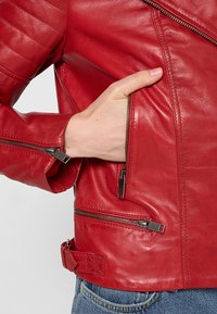 Chaqueta de cuero roja con detalles acolchados en los hombros, cremalleras plateadas y un bolsillo lateral. Presenta una cintura con cinturón para un ajuste ajustable.