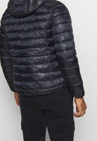 Czarna kurtka puchowa o błyszczącej powierzchni, z poziomymi paskami, kapturem i teksturowanym wzorem. Rękawy są dopasowane i elastyczne.