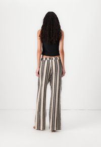 Loose, high-waisted, wide-leg pants in cream with black vertical stripes, featuring a textured fabric and elastic waistband.