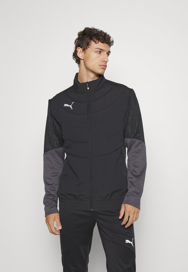 Schwarze Zip-Jacke mit strukturiertem Design, grauen Ärmeln und reflektierendem Puma-Logo; gefertigt aus glattem, leichtem Material.