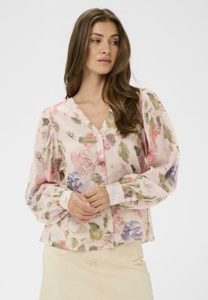 Bloemenblouse van lichtroze stof met groene en paarse patronen. Voorzien van een V-hals, lange pofmouwen en knoopsluitingen.