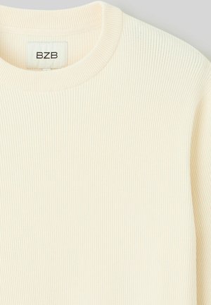 Pull en maille côtelée couleur crème avec un col rond. L'étiquette affiche "BZB". Le tissu a une texture douce et un motif vertical subtil.