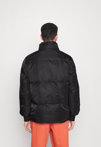 Giacca nera imbottita con colletto alto, caratterizzata da una texture lucida e liscia e pannelli trapuntati distribuiti in modo uniforme.