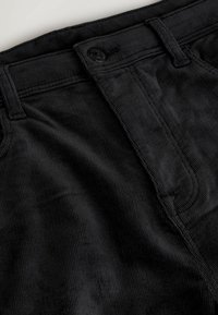 Black corduroy pants featuring vertical ribbed texture, front pockets, a button closure, and a stitched waistband.