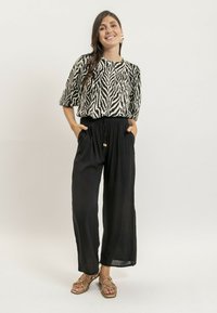 Blouse à imprimé zèbre noir et blanc avec des manches courtes, associée à un pantalon large noir avec taille à cordon et poches. Sandales dorées.