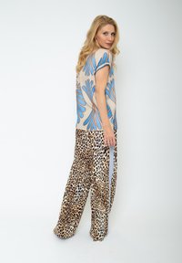 Lekki beżowy top z niebieskim kwiatowym wzorem, zestawiony z luźnymi spodniami w panterkę z bocznymi paskami. Gładki materiał z szerokimi nogawkami.