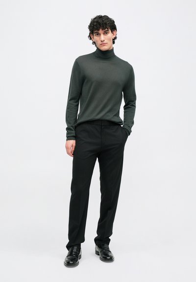 Temno zelena pulover s turtleneckom, v kombinaciji z črnimi hlačami in črnimi čevlji, z ozkim krojem in gladko teksturo. Enostavna zasnova, brez vzorcev.