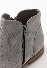 Harmaat mokkasiinipohjaiset nilkkasaappaat, joissa on teksturoitu pinta, sivuvetoketjusuljenta ja puinen korko. Ominaisuuksiin kuuluu hienovaraista ompelua ja pyöreä kärki.