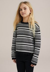 Svart och vit randig stickad tröja med ribbade kanter och vågiga fållar. Har långa ärmar och en rund halsringning.