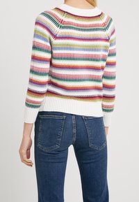 Suéter de punto con rayas horizontales multicolores, cuello y puños blancos, dobladillo acanalado, combinado con jeans oscuros, mostrando un ajuste relajado.