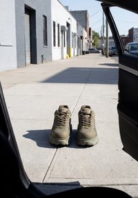 Deux baskets beige placées côte à côte sur un trottoir urbain vide, vues depuis une portière de voiture ouverte.